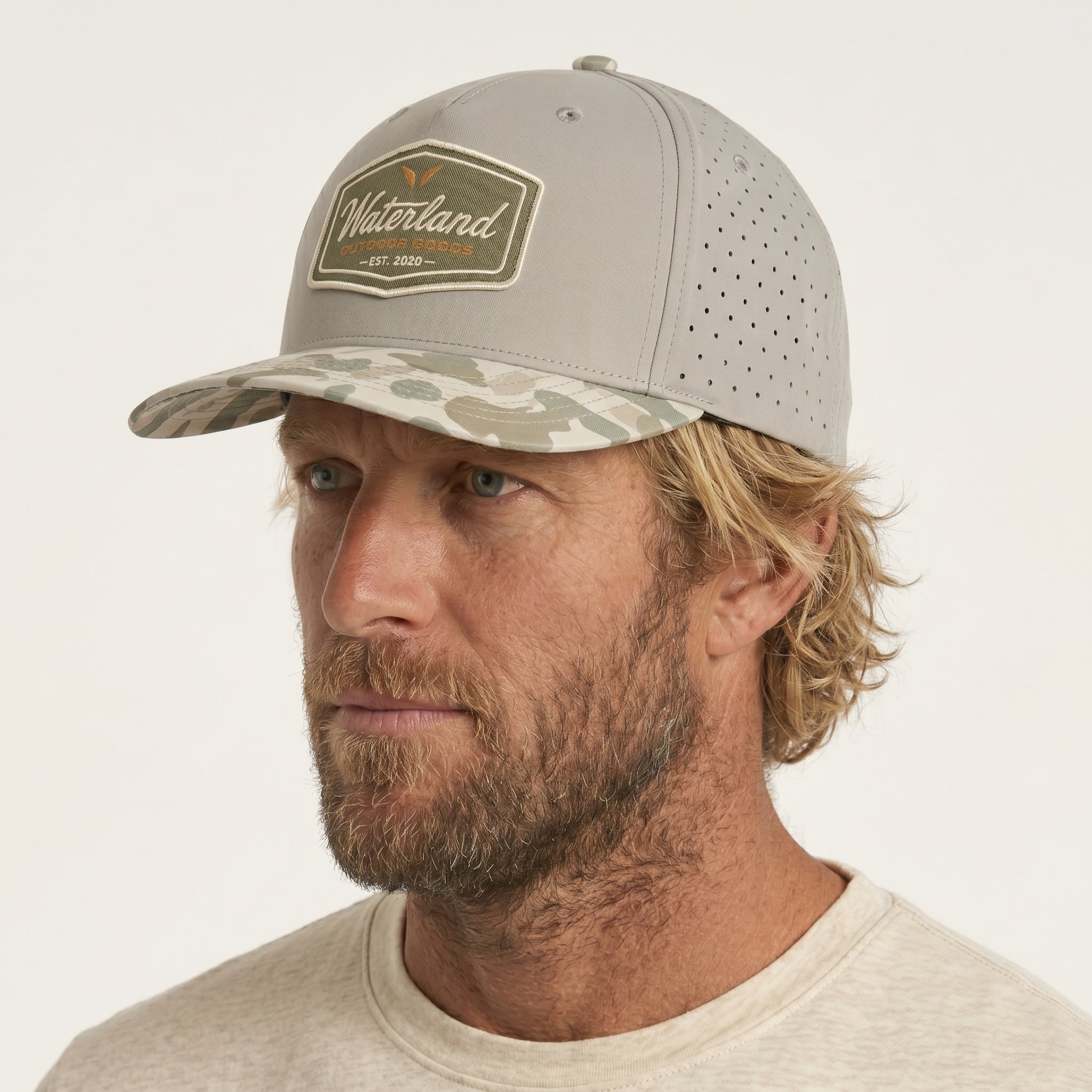 Man wearing a gray cap with a camouflage bill and Waterland logo on a white background