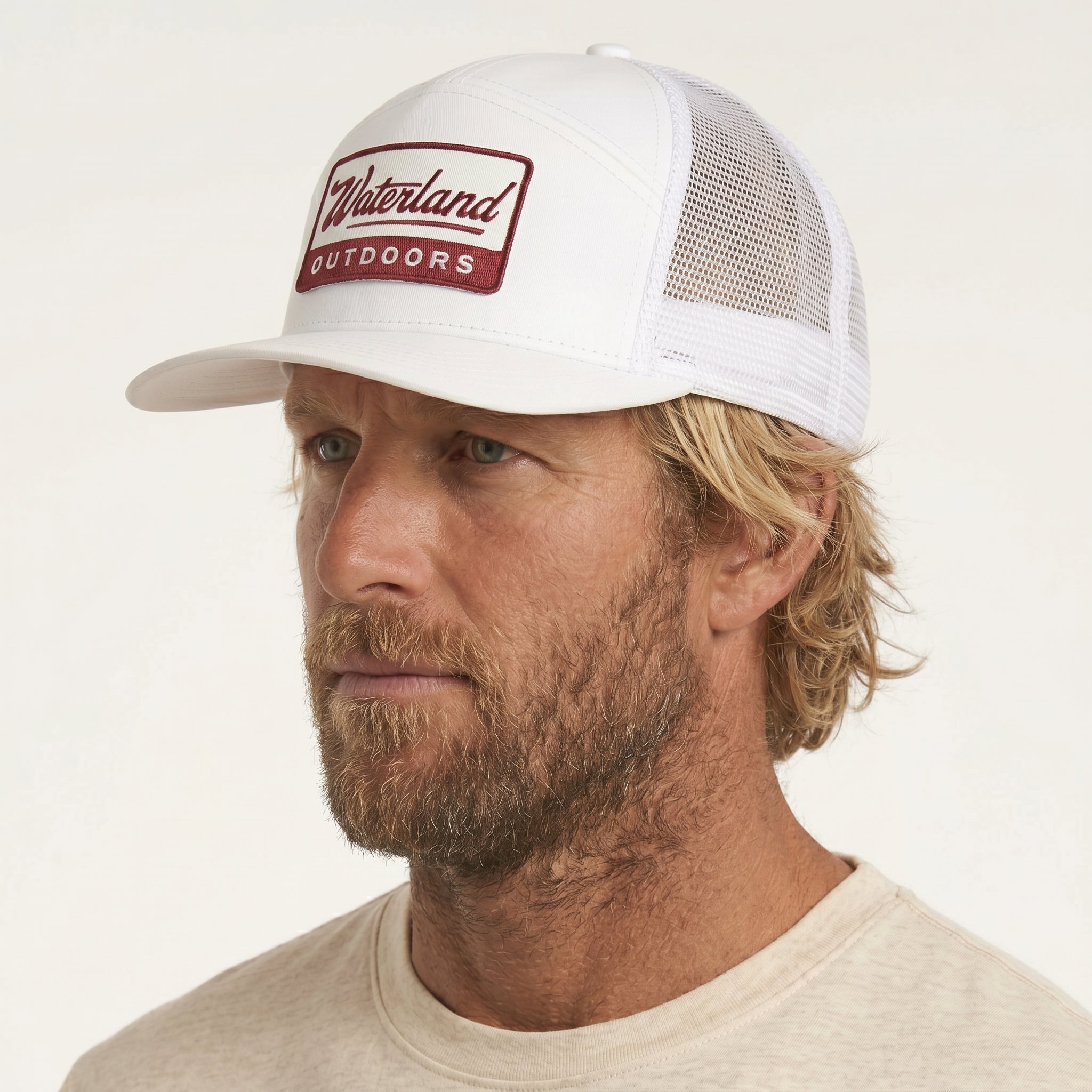 Man wearing a white cap with 'Waterland Outdoors' logo on a beige background