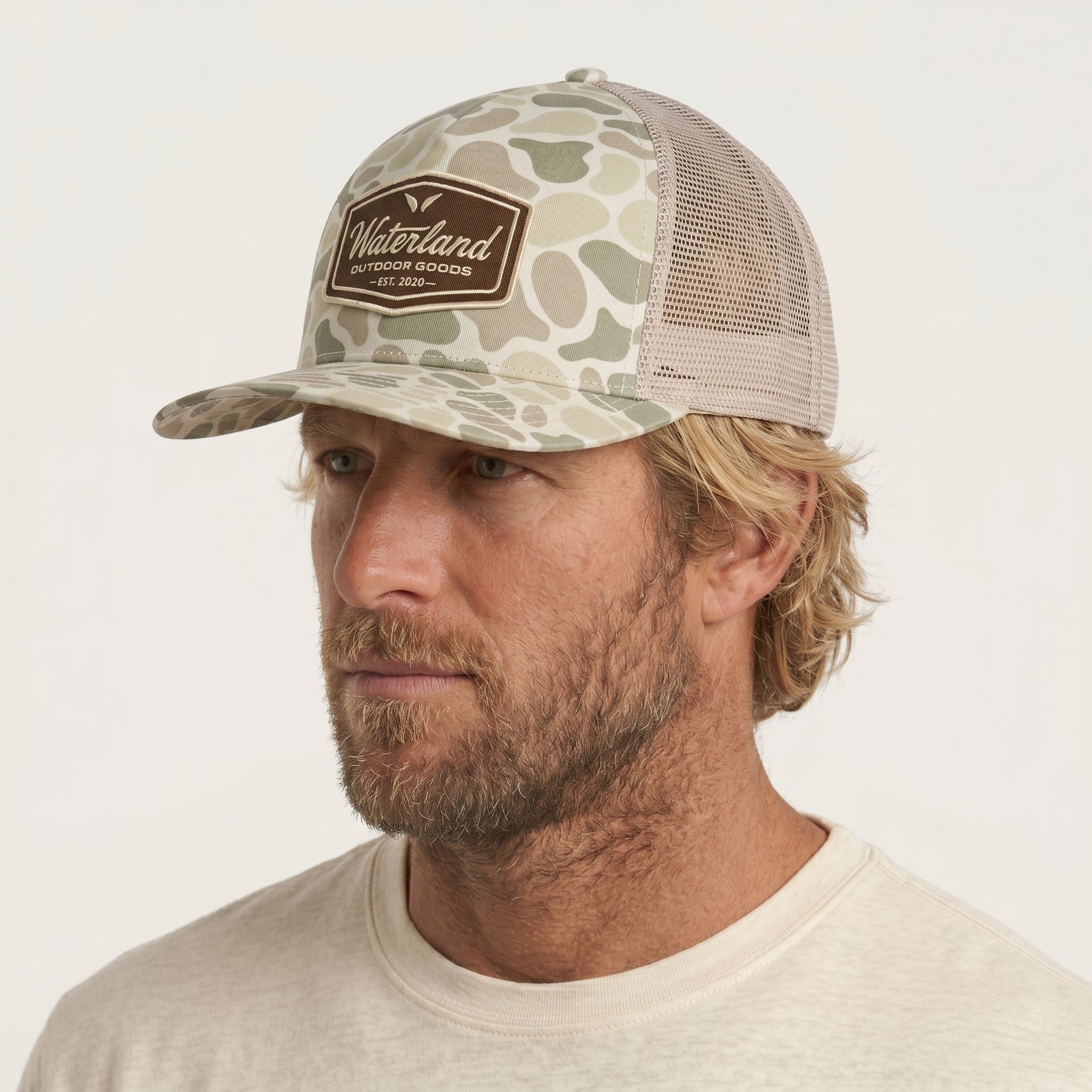 Man wearing a camouflage cap with a brand logo on a white background